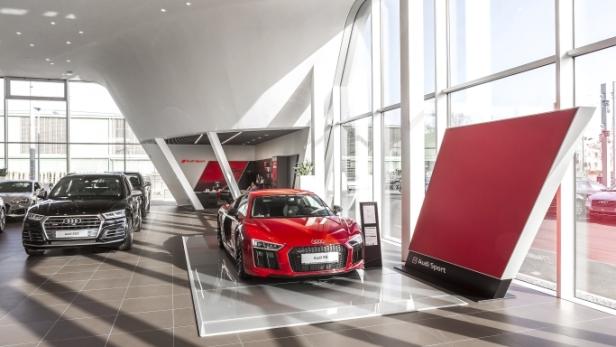 In einem hellen Audi-Autohaus stehen mehrere Neuwagen, darunter ein roter Audi R8.