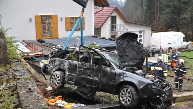 Ein schwer beschädigtes Auto wird von einem Kran vor einem Haus angehoben.