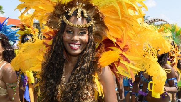 Eine lächelnde Frau mit einem gelb-roten Federkopfschmuck und Karnevalskostüm.