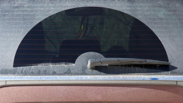 Die Heckscheibe eines schmutzigen Autos mit einem Scheibenwischer.
