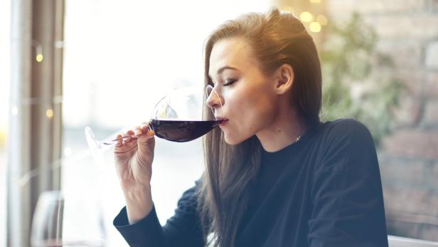 Frau trinkt Rotwein aus langstieligem Glas