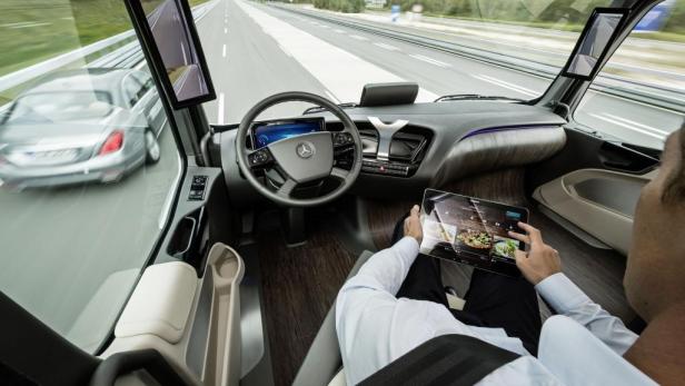 Ein Mann sitzt in einem selbstfahrenden Mercedes-Lkw und bedient ein Tablet.