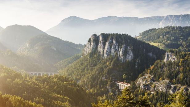 Blick auf die Semmeringbahn, die sich durch eine grüne Berglandschaft schlängelt.