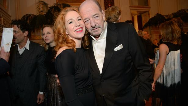 Eine Frau mit roten Haaren umarmt einen älteren Mann im Smoking.