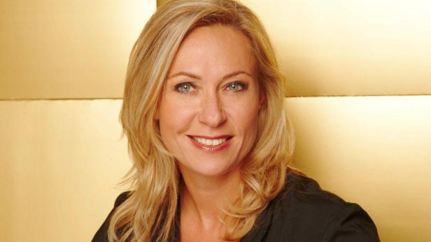 Eine lächelnde Frau mit blonden Haaren vor einem goldenen Hintergrund.