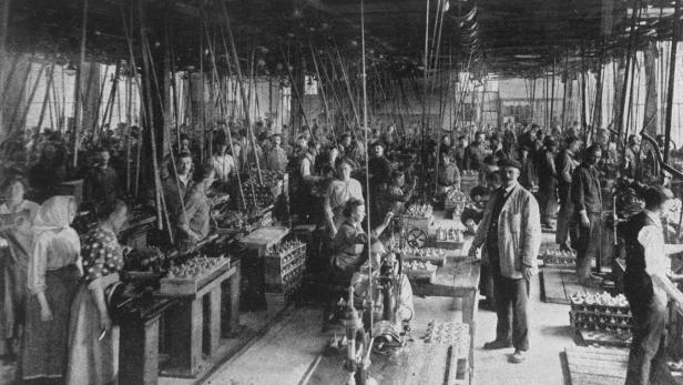 Historische Aufnahme einer Fabrikhalle mit zahlreichen Arbeiterinnen und Arbeitern an ihren Arbeitsplätzen.