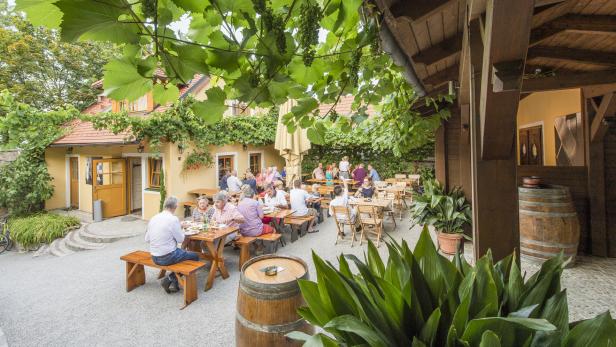 Ein Heuriger mit Gästen, die unter Weinreben sitzen und essen.