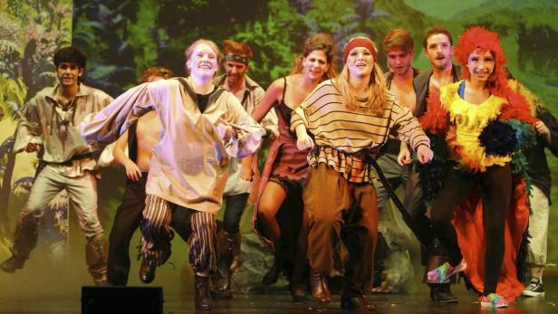 Eine Gruppe von Darstellern in Kostümen steht auf einer Bühne vor einem Dschungelhintergrund.