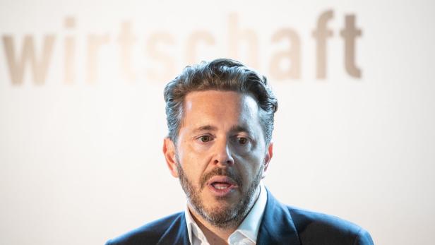 Ein Mann im Anzug spricht vor einem Hintergrund mit dem Wort „wirtschaft“.