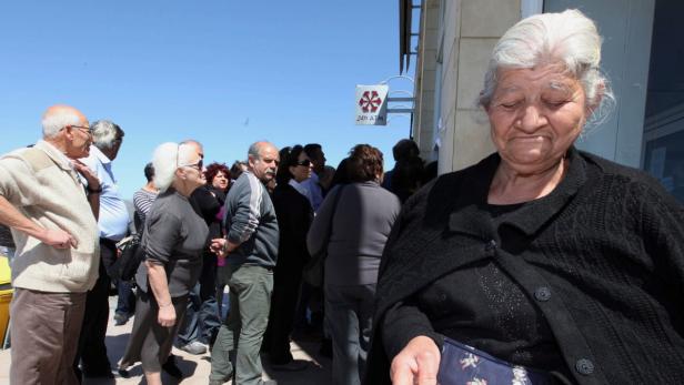 epa03643364 An elderly woman (R) looks at a savings book as people wait in line in front of a branch of the Laik Bank in Nicosia, Cyprus, 28 March 2013. All of the country&#039;s 26 banks were open from 12 pm until 6 pm (1000-1600 GMT) on 28 March with a withdrawal limit set at 300 euros (383 dollars) per person. Cyprus was braced for the reopening of its banks after nearly two weeks, after the government imposed tough capital controls for at least the next seven days. Police were going from bank to bank in central Nicosia to prevent problems, while dozens of people had started to queue in front of the banks&#039; doors. EPA/KATIA CHRISTODOULOU