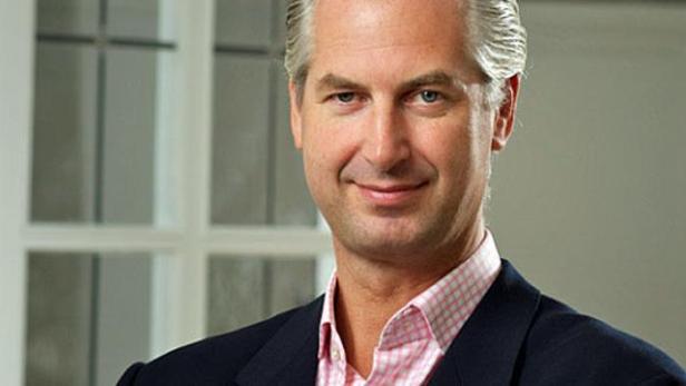 Ein Mann mit grauem Haar und einem rosa Hemd lächelt in die Kamera.