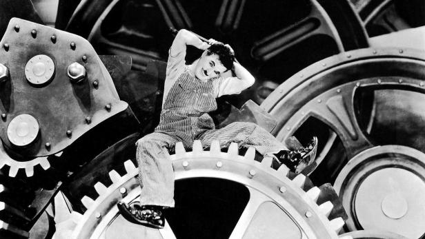 Charlie Chaplin sitzt inmitten von riesigen Zahnrädern.