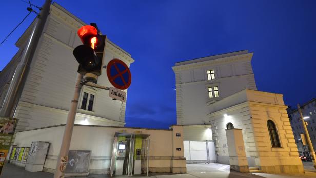 Eine rote Fußgängerampel vor zwei weißen Gebäuden in Wien bei Nacht.