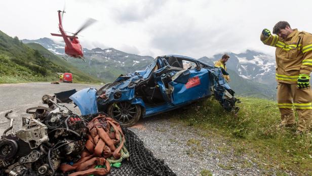 Ein schwer beschädigtes blaues Auto nach einem Unfall in den Bergen, ein Rettungshubschrauber ist im Einsatz.
