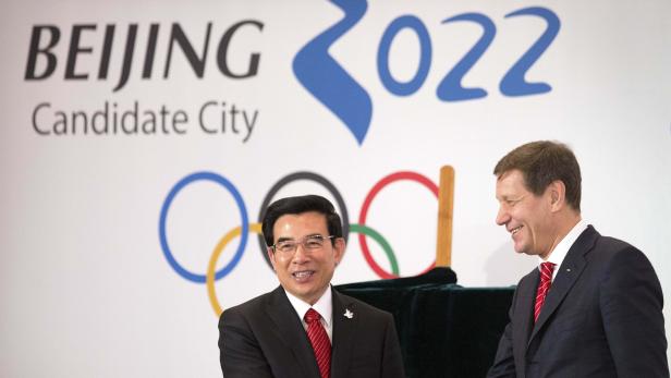 Zwei Männer stehen vor einem Banner für die Olympischen Winterspiele 2022 in Peking.