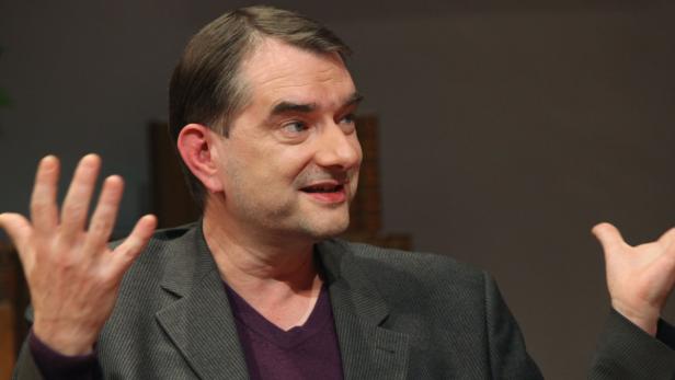 Ein Mann in einem grauen Sakko gestikuliert mit beiden Händen.