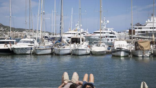 Ein Paar entspannt am Hafen, im Hintergrund zahlreiche Segelboote und Yachten.