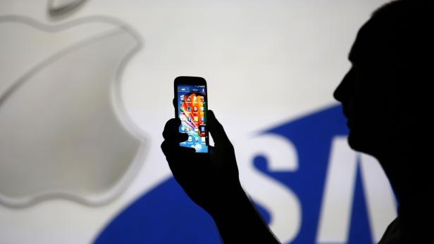 File photo illustration of a man is silhouetted against a video screen with Apple and Samsung logos while posing with a Samsung S4 smartphone in Zenica
