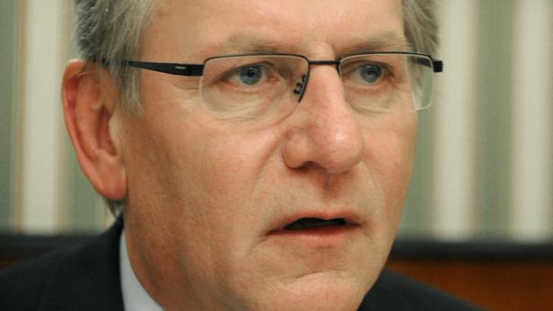 Ein Mann mit grauen Haaren, Anzug und Krawatte schaut aufmerksam zur Seite.