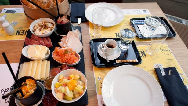 Ein Tisch mit einem Frühstücks- oder Brunch-Arrangement mit Brot, Aufschnitt, Käse und Obstsalat.