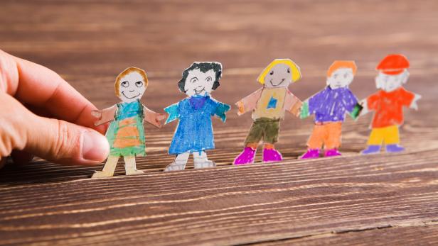 the child does figures of people of paper. Paper people on wooden background. Creative child play with craft.