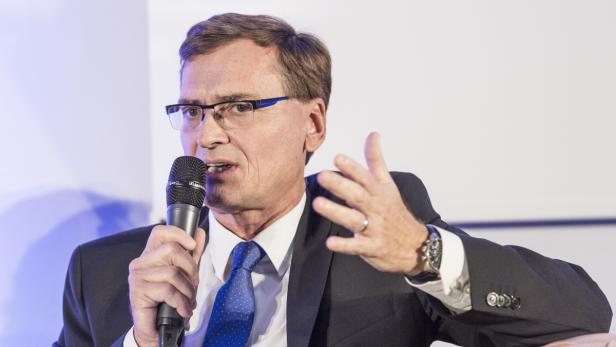 Ein Mann mit Brille und Anzug spricht in ein Mikrofon und gestikuliert.