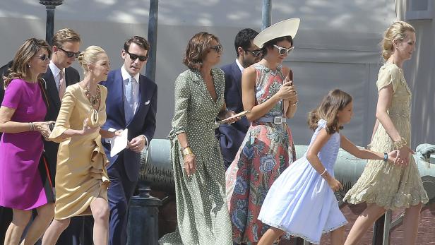 Eine Gruppe elegant gekleideter Menschen geht an einem sonnigen Tag entlang.