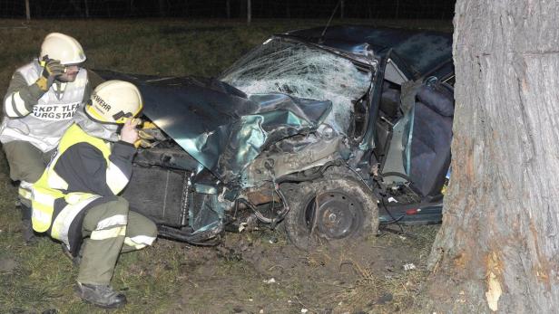 Ein Auto ist gegen einen Baum gefahren, zwei Feuerwehrleute begutachten den Schaden.