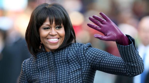 Michelle Obama lächelt und winkt mit einem lilafarbenen Handschuh.