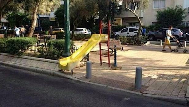 Ein gelbe Rutsche steht auf einem Spielplatz in einer städtischen Umgebung.