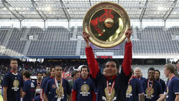 Ein Fußballspieler hält die Meisterschale in die Höhe, umgeben von seinen Teamkollegen.