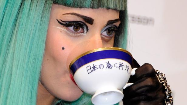 Lady Gaga mit türkisfarbenem Haar trinkt aus einer Teetasse mit japanischer Schrift.