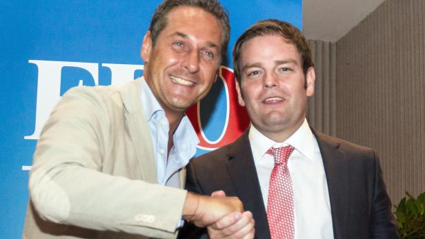 Zwei Männer in Anzügen geben sich die Hand vor einem blauen Hintergrund.