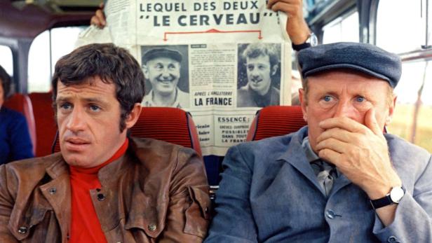 Jean-Paul Belmondo und Bourvil sitzen in einem Bus, hinter ihnen eine Zeitung mit dem Titel „Le Cerveau“.
