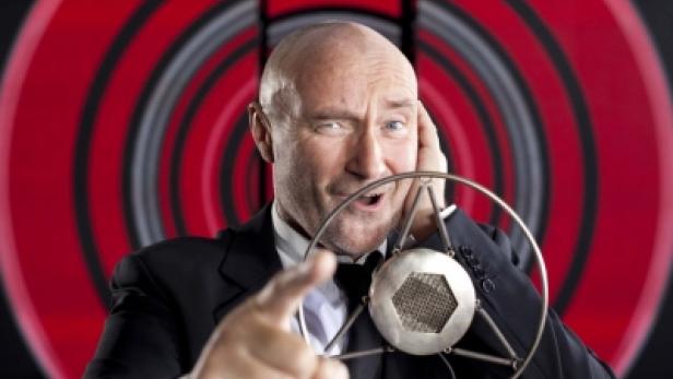 Phil Collins posiert mit einem alten Mikrofon vor einem roten Hintergrund.