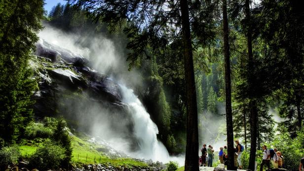 Eine Gruppe von Menschen betrachtet einen hohen Wasserfall im Wald.