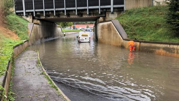 Ein überfluteter Tunnel mit einem Arbeiter in oranger Kleidung und einem Lieferwagen.