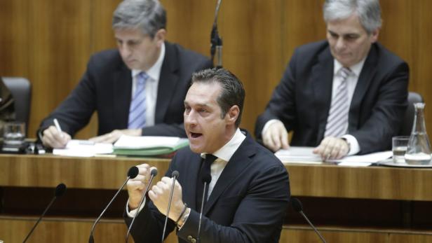 Ein Mann gestikuliert während einer Rede vor Mikrofonen.