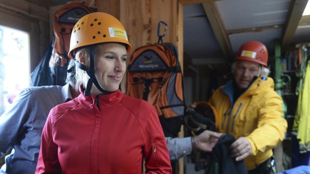 Eine Frau mit roter Jacke und Helm steht in einem Raum mit Ausrüstung.