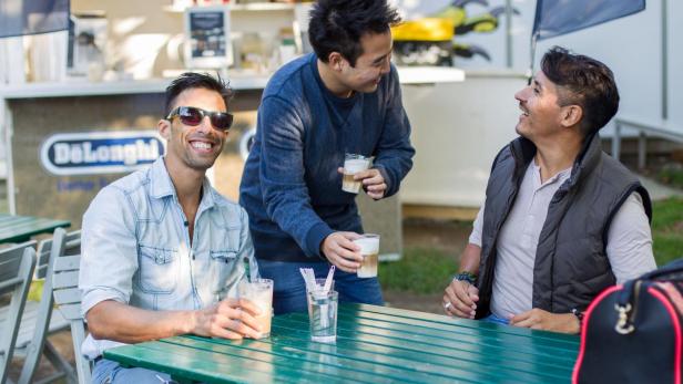 Drei Männer sitzen an einem Tisch und trinken Kaffee.