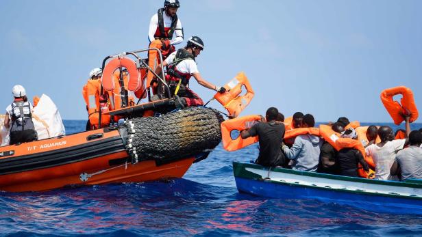Mitglieder von SOS Mediterranee und Ärzte ohne Grenzen übergeben Schwimmwesten an Flüchtlinge auf Holzboot.