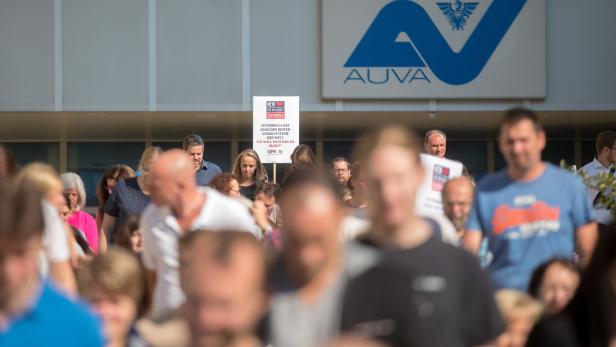 Eine Menschenmenge demonstriert vor einem Gebäude der AUVA mit einem Schild zum österreichischen Sozialsystem.