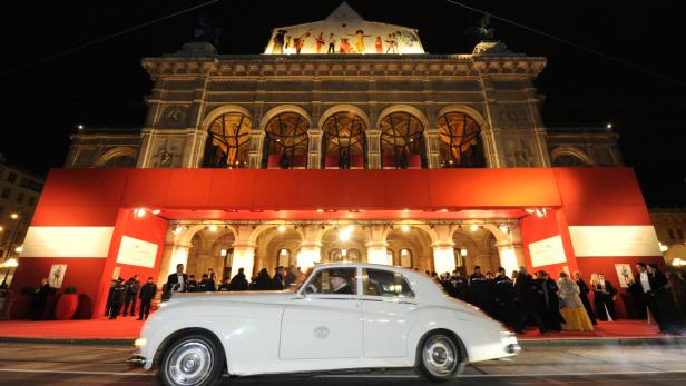Ein weißes Auto fährt vor der Wiener Staatsoper auf dem roten Teppich vor.