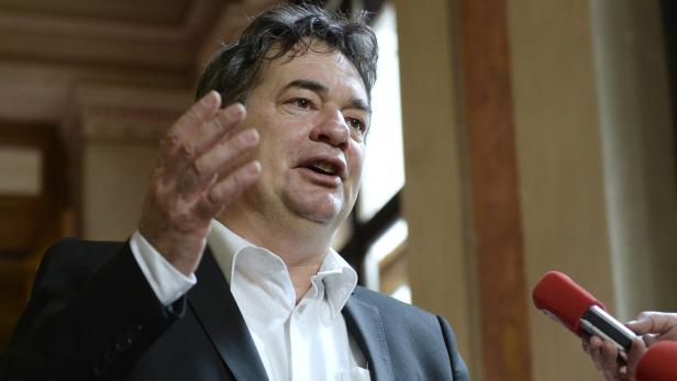 Ein Mann in Anzug gestikuliert während eines Interviews vor Mikrofonen.