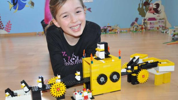 Ein lächelndes Mädchen liegt vor einem gelb-schwarzen Lego-Pinguin-Karussell.