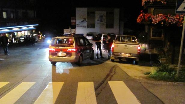 Ein Polizist kontrolliert in der Nacht ein Auto auf einer dunklen Straße.
