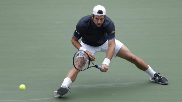 Ein Tennisspieler schlägt einen Ball auf einem grünen Platz.