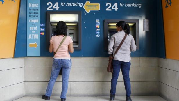 Women withdraw money from ATMs at a branch of the Bank of Cyprus at Eleftheria square in Nicosia March 30, 2013. Major depositors in Cyprus&#039;s biggest bank will lose around 60 percent of savings over 100,000 euros, its central bank confirmed on Saturday, sharpening the terms of a bailout that has shaken European banks and saved the island from bankruptcy. Initial signs that big depositors in Bank of Cyprus would take a hit of 30 to 40 percent - the first time the euro zone has made bank customers contribute to a bailout - had already unnerved investors in European lenders this week. REUTERS/Bogdan Cristel (CYPRUS - Tags: BUSINESS POLITICS)