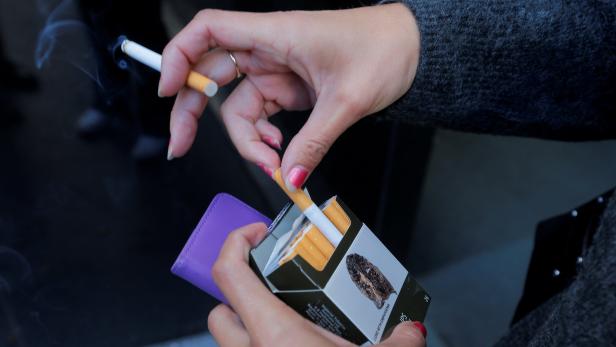 FILE PHOTO: A photo illustration shows a smoker with a pack of cigarettes featuring restrictive tobacco packaging outside a Sydney office building in Australia