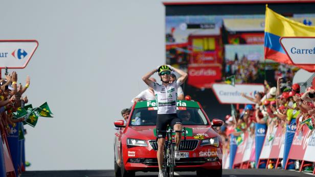 Ein Radfahrer feiert seinen Sieg bei der Vuelta a España, begleitet von einem roten Skoda-Begleitfahrzeug.